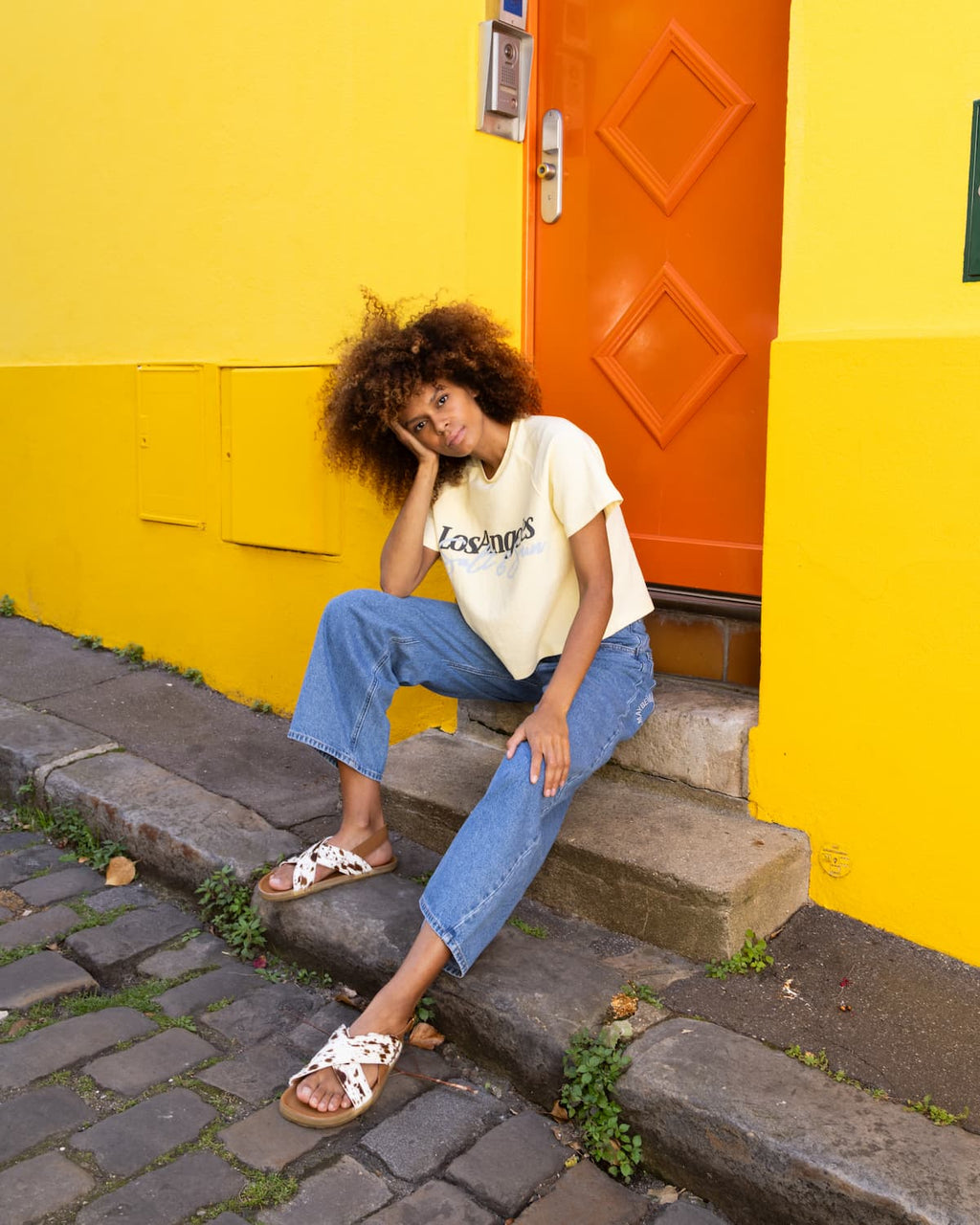 Woman sitting on steps in front of a yellow wall with an orange door