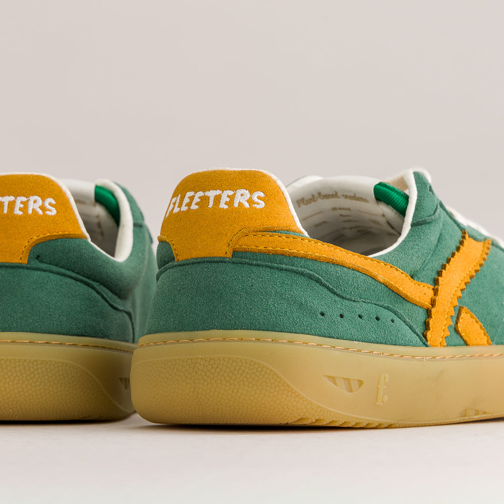 A pair of suede low-top sneakers shown from the back, featuring a dark green suede upper, mustard yellow heel tabs with white 'FLEETERS' branding, a yellow side stripe, and a beige gum sole.