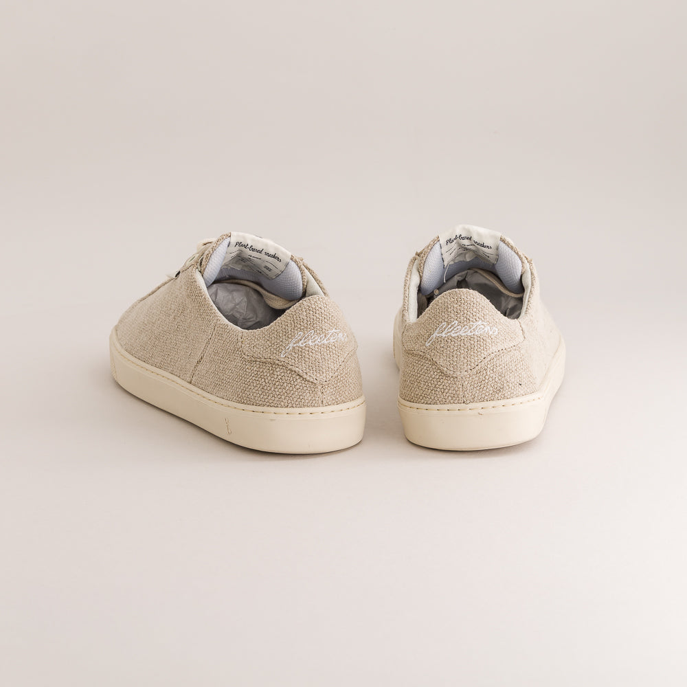 A pair of beige wool barefoot sneakers shown from the back on a light beige background.