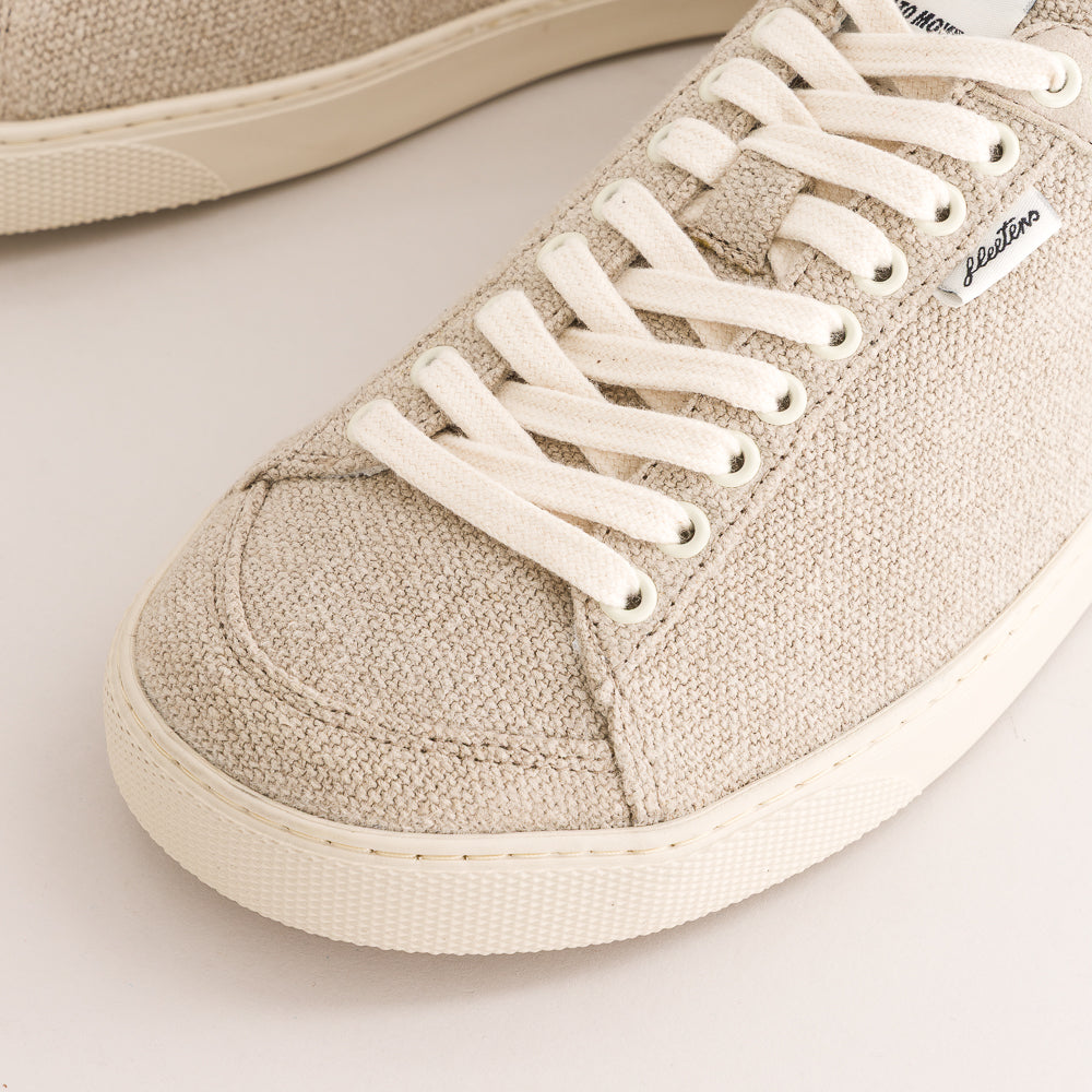 Close-up of a beige wool low-top sneaker with white laces and a white rubber sole, showing the side panel and a small white brand tag.