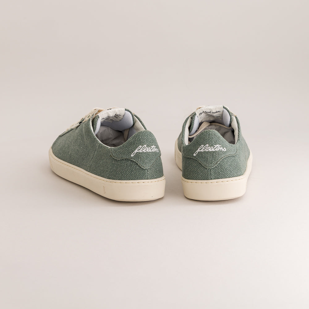 A pair of green canvas low-top sneakers shown from the back, featuring white soles and the brand name 'fleeters' embroidered on the heel, set against a plain light beige background.
