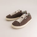 A pair of low-top wool sneakers in dark brown with off-white laces and soles, displayed on a light beige studio background.