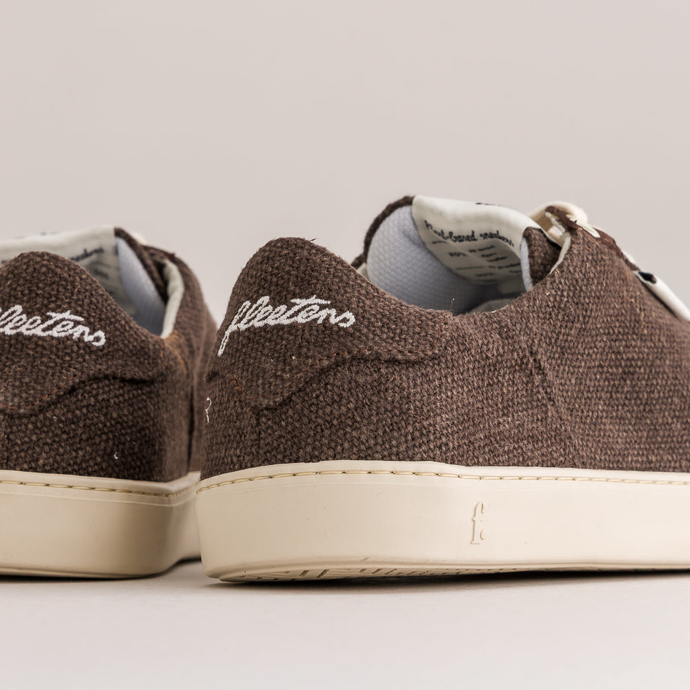 Close-up of a pair of brown canvas low-top sneakers with white soles and white embroidered 'fleeters' branding on the heel, shown against a light gray background.