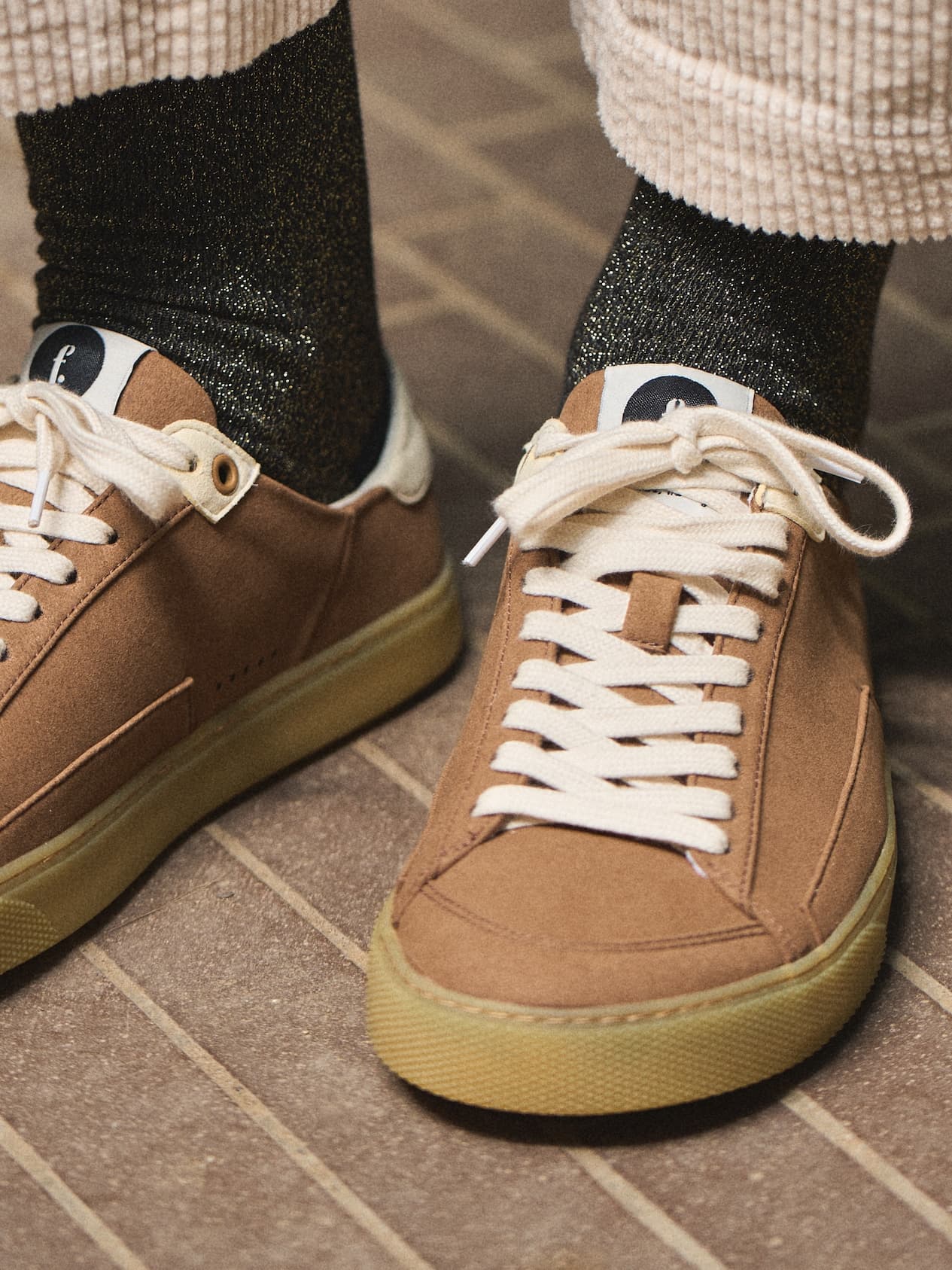 Brown barefoot sneakers with white laces worn on a tiled floor