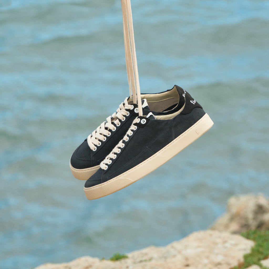 Black sneakers with white soles hanging against a blue water background