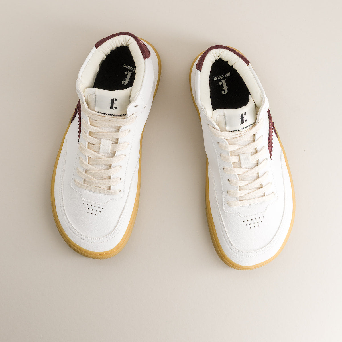 Pair of white barefoot sneakers with brown accents on a beige background