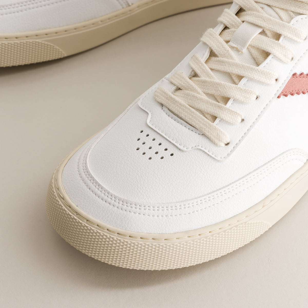 Close-up of a white sneaker with beige laces on a light background