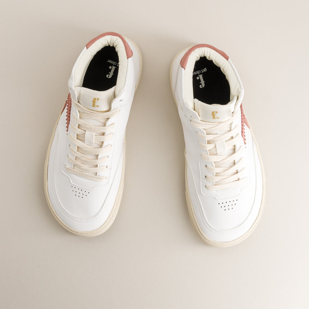 Pair of white mid-ankle barefoot sneakers with pink accents on a beige background