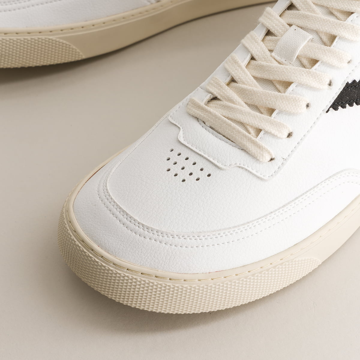 Close-up of a white sneaker with beige accents on a light background