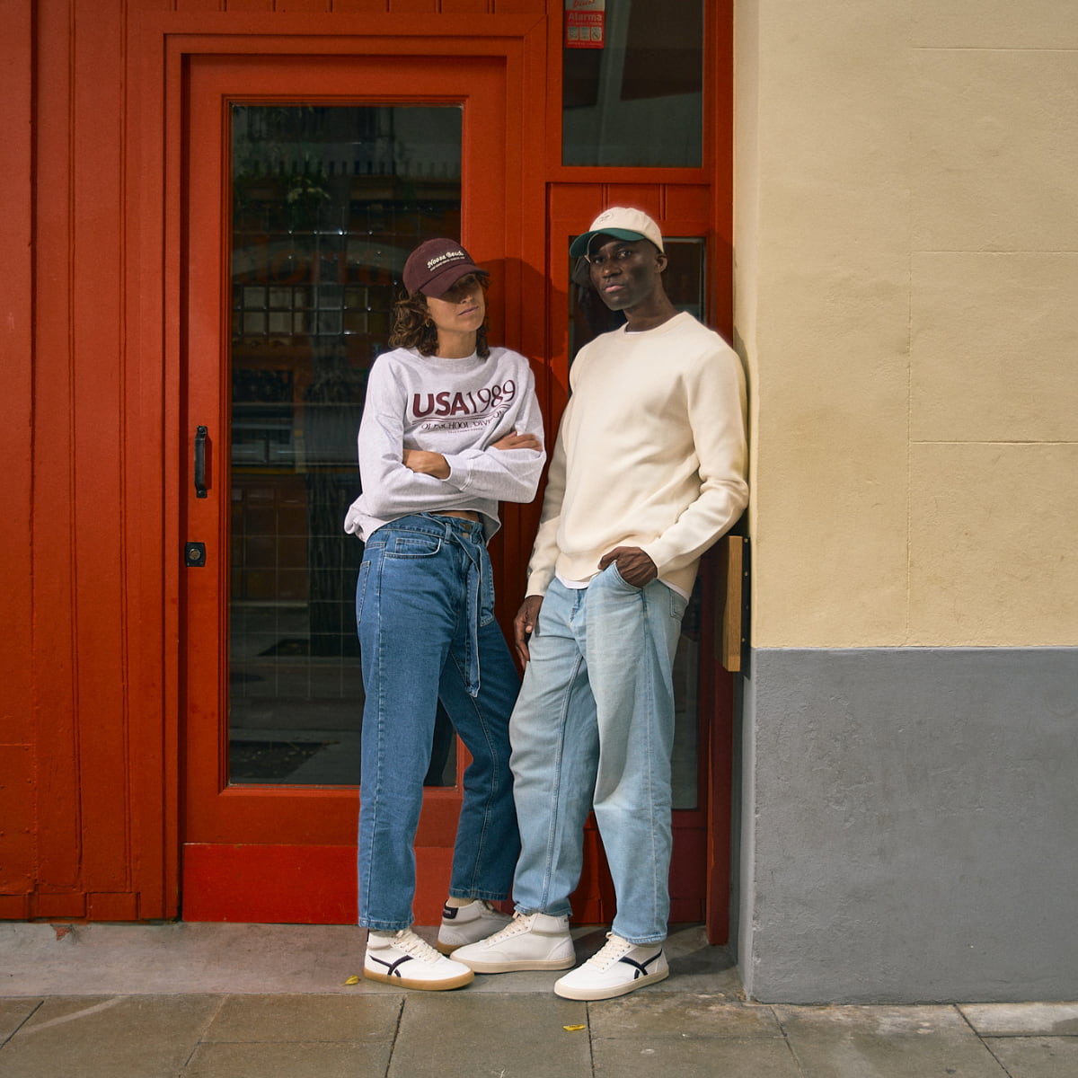 Two people standing in front of a red door wearing White high-top barefoot sneaker with black design.