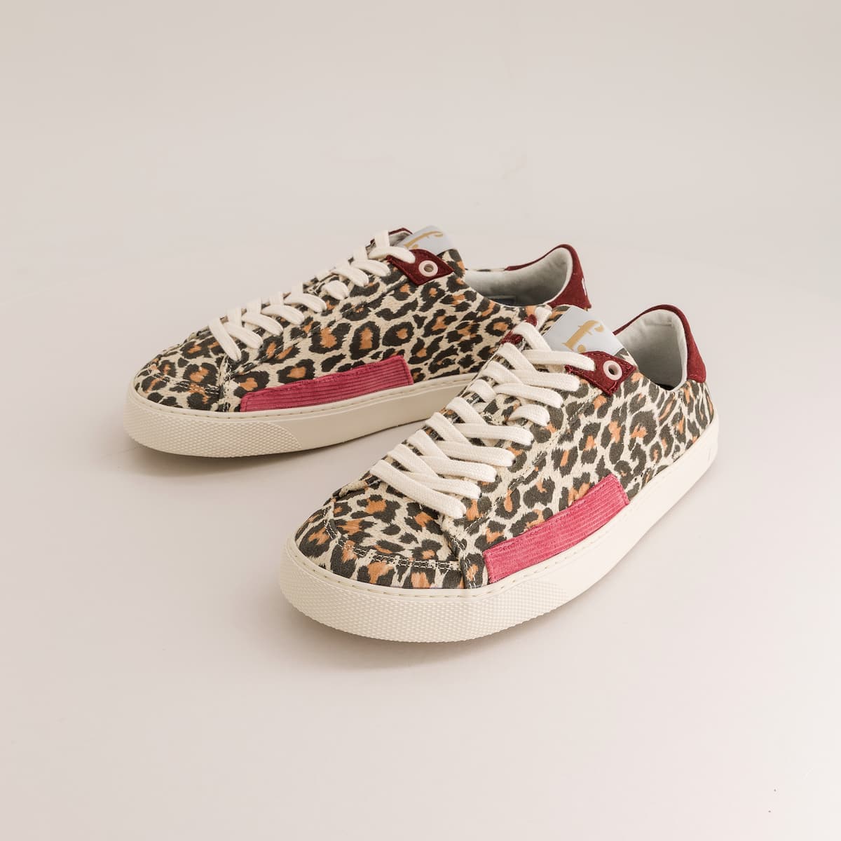 A pair of low-top barefoot canvas sneakers featuring a leopard print pattern, white laces, a pink side stripe, and a burgundy heel tab, displayed on a light gray background.