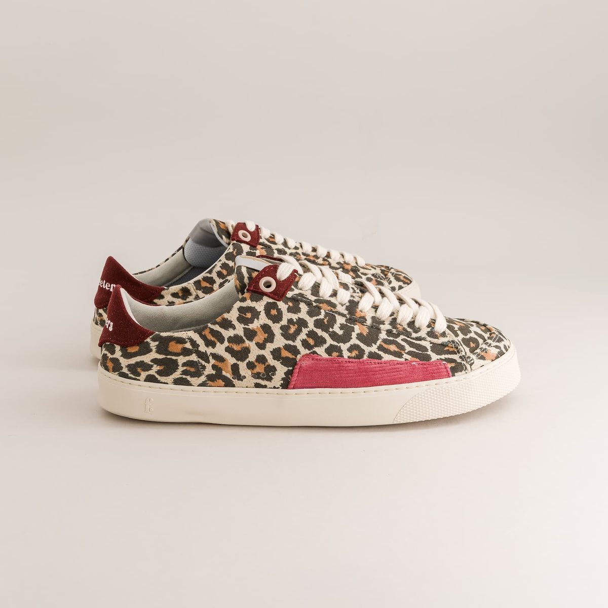 A pair of low-top barefoot sneakers featuring a leopard print pattern in beige, brown, and black, with a bright pink side panel and a dark red heel tab, set against a plain light gray background.