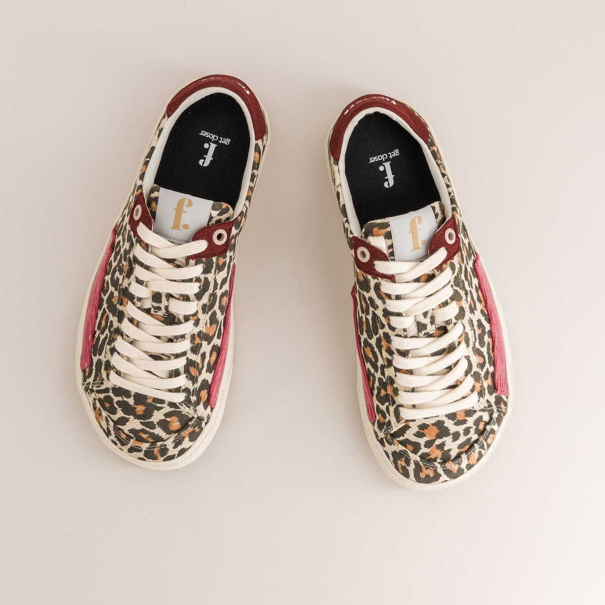 A pair of low-top barefoot sneakers shown from a top-down view on a light beige background. The shoes feature a leopard print pattern in brown, black, and beige, with white laces, white rubber soles, and burgundy leather trim around the collar and side panels.