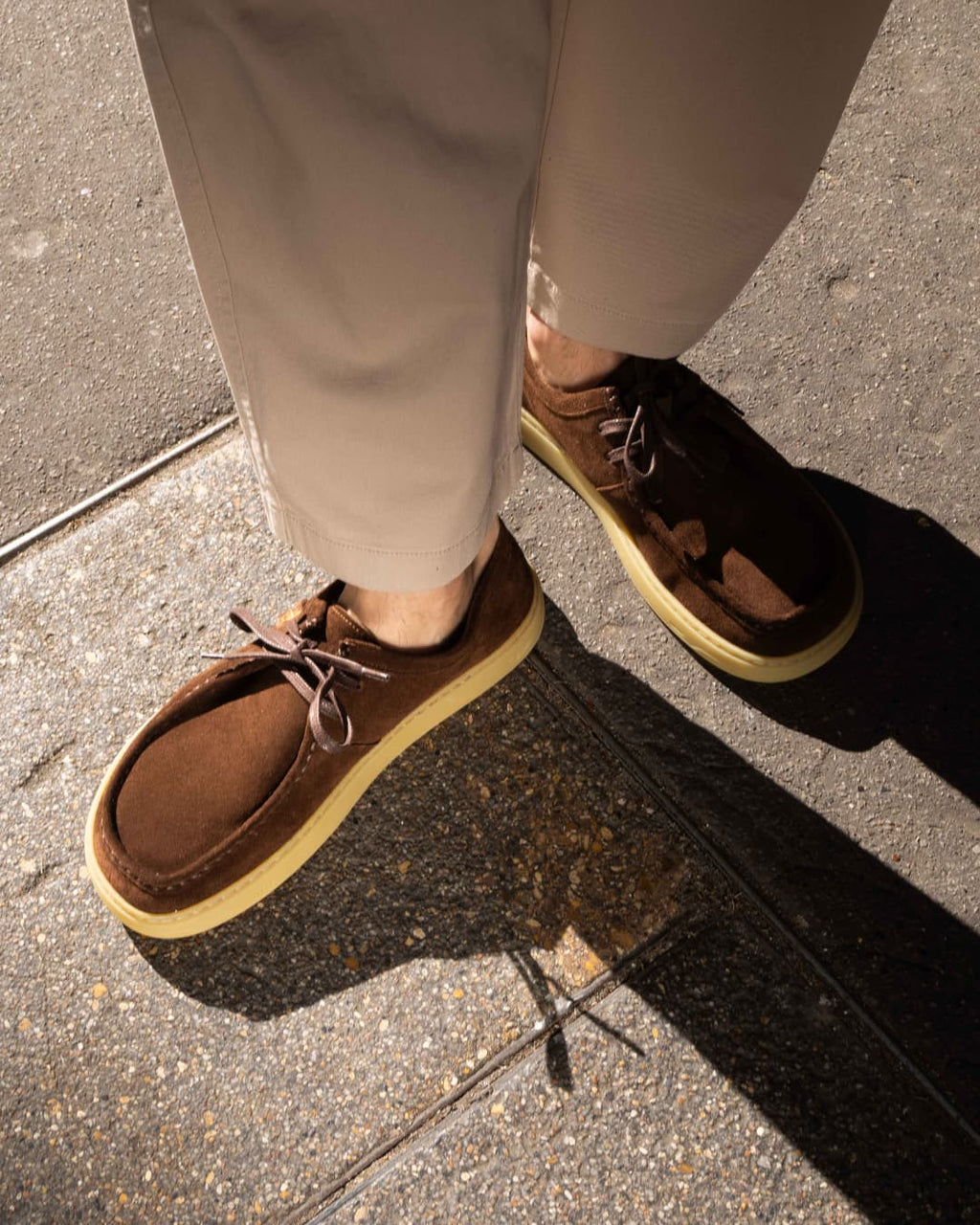 Brown barefoot derbies with yellow soles worn on a sidewalk