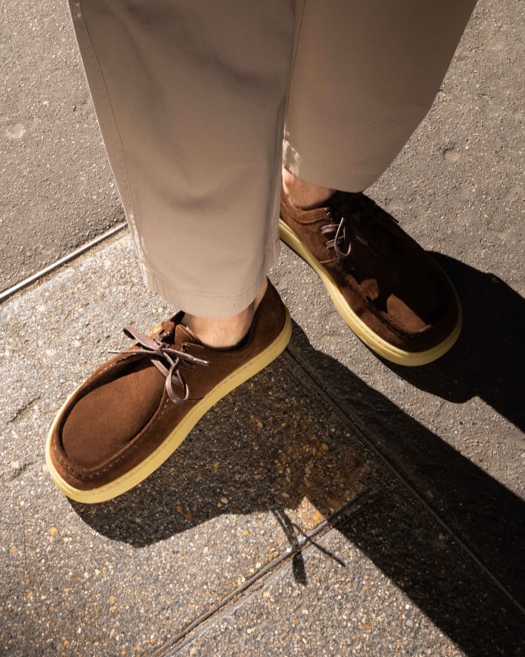 Brown barefoot derbies with yellow soles worn on a sidewalk
