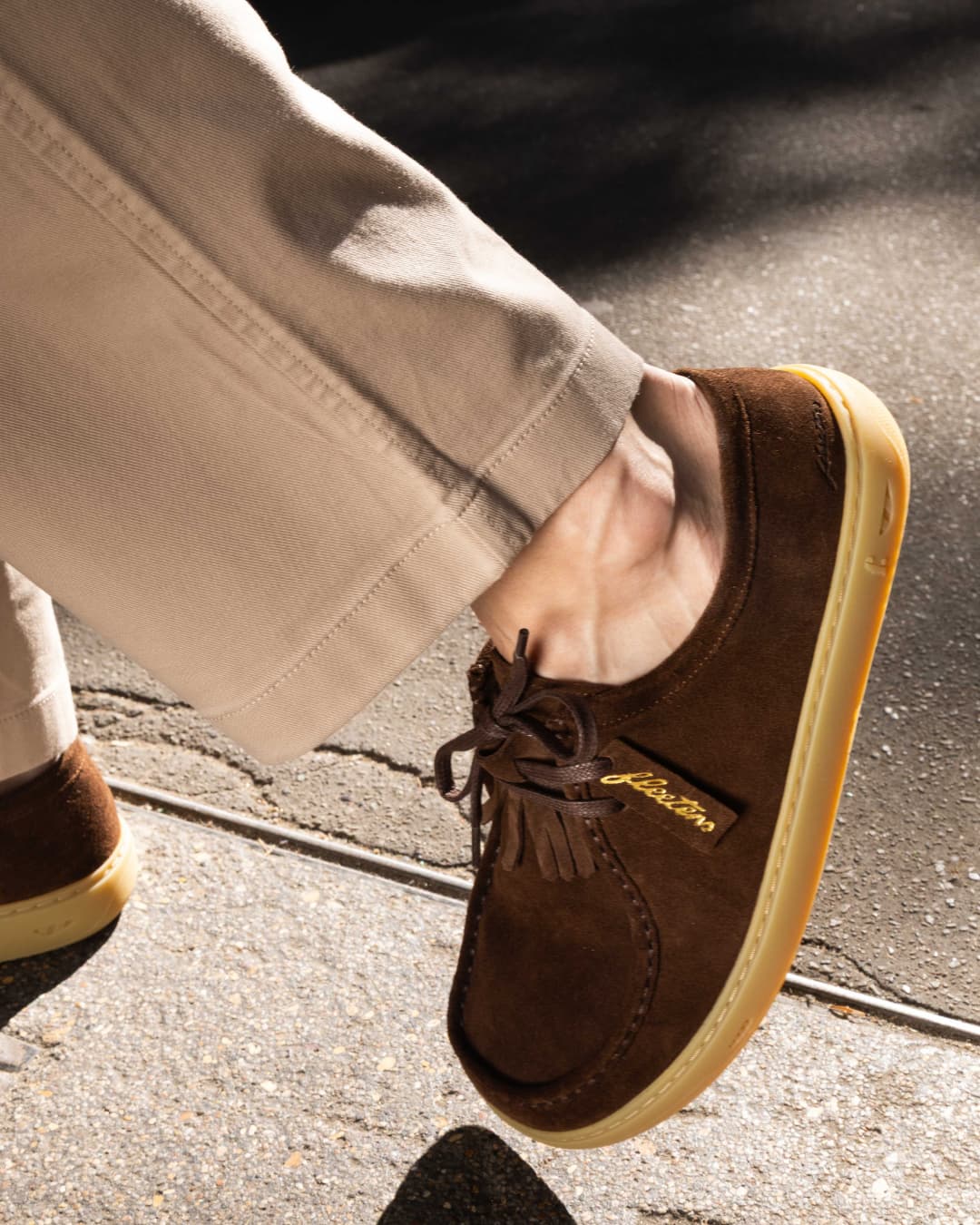 Brown suede shoes with a brand logo on a concrete surface