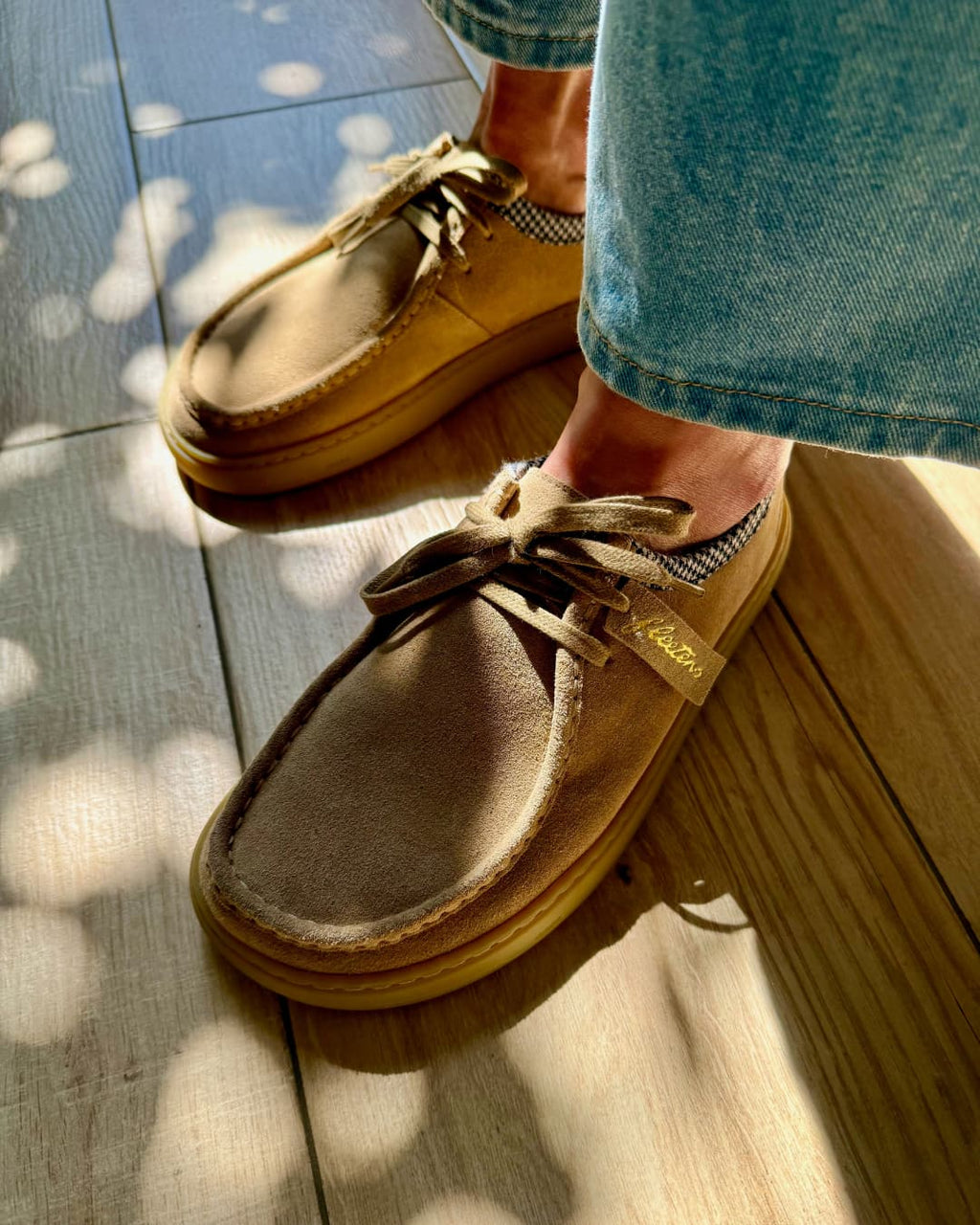 Tan barefoot derby shoes worn with denim jeans on a wooden floor.