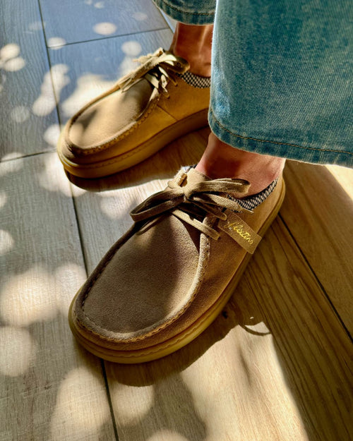 Tan barefoot derby shoes worn with denim jeans on a wooden floor.