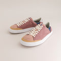 A pair of barefoot sneakers in dusty pink suede with tan leather toe caps, white laces, and white rubber soles, photographed on a light beige background.