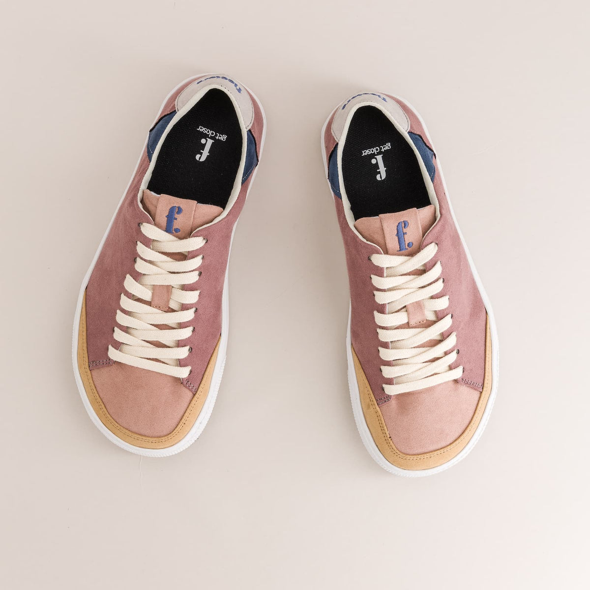 A pair of low-top barefoot sneakers shown from a top-down view on a light beige background. The shoes feature dusty pink suede and canvas panels, cream-colored laces, a tan midsole stripe, and a white rubber sole.