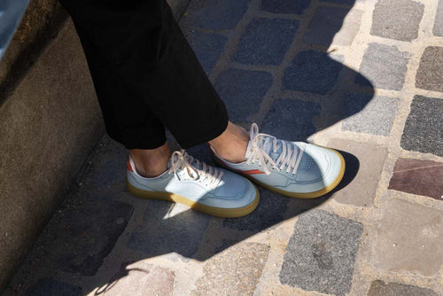 Light blue barefoot sneakers with white laces worn on a stone pavement