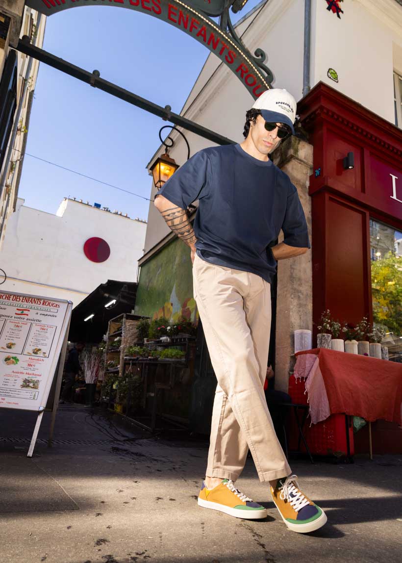 Person wearing a navy t-shirt, beige pants, and colorful sneakers standing on a street with a building and sign in the background.