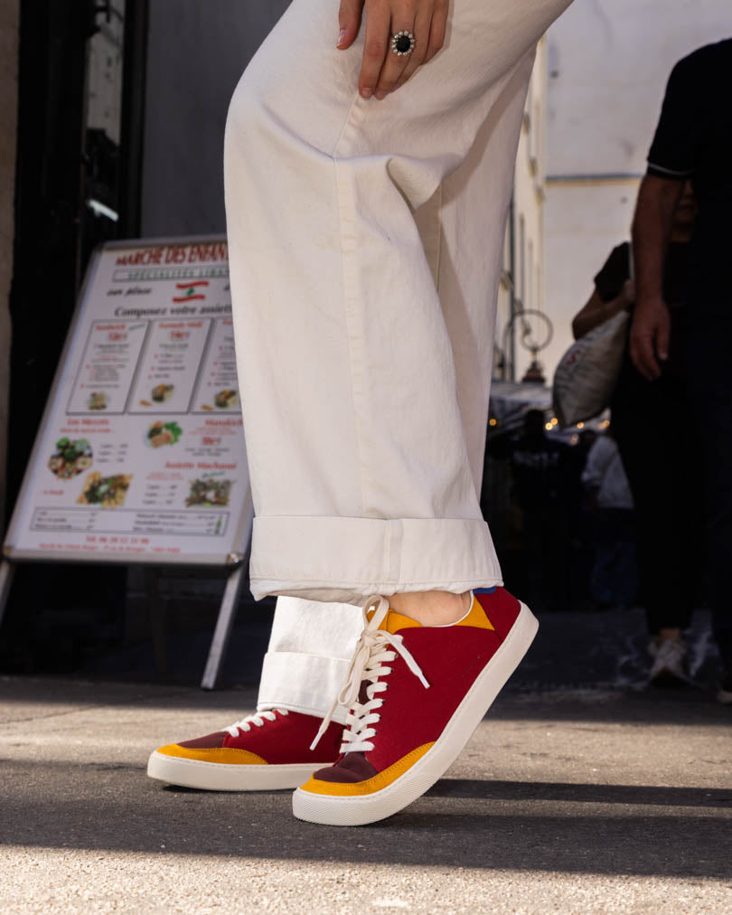 Red and yellow barefoot sneakers worn with white pants on a street.