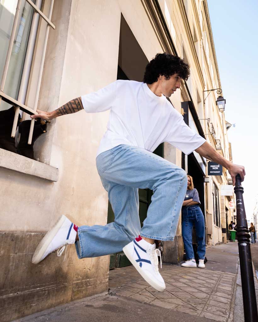 Person in white shirt and blue jeans jumping on a city street