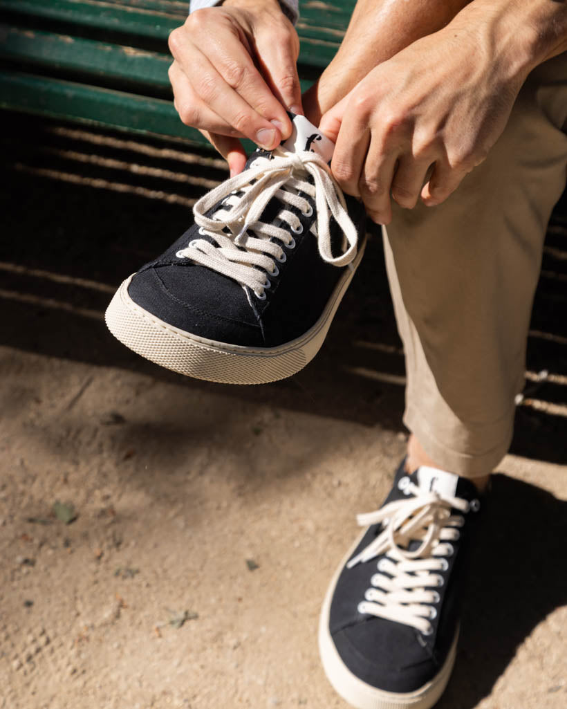 Person tying the laces of a black sneaker on a concrete surface.