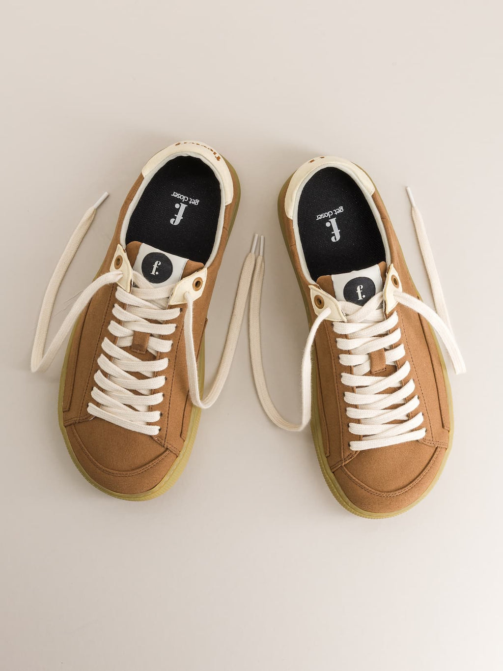 Pair of tan minimalist sneakers with white laces on a light gray background